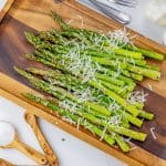 cooked asparagus topped with shredded parmesan cheese on a wooden platter