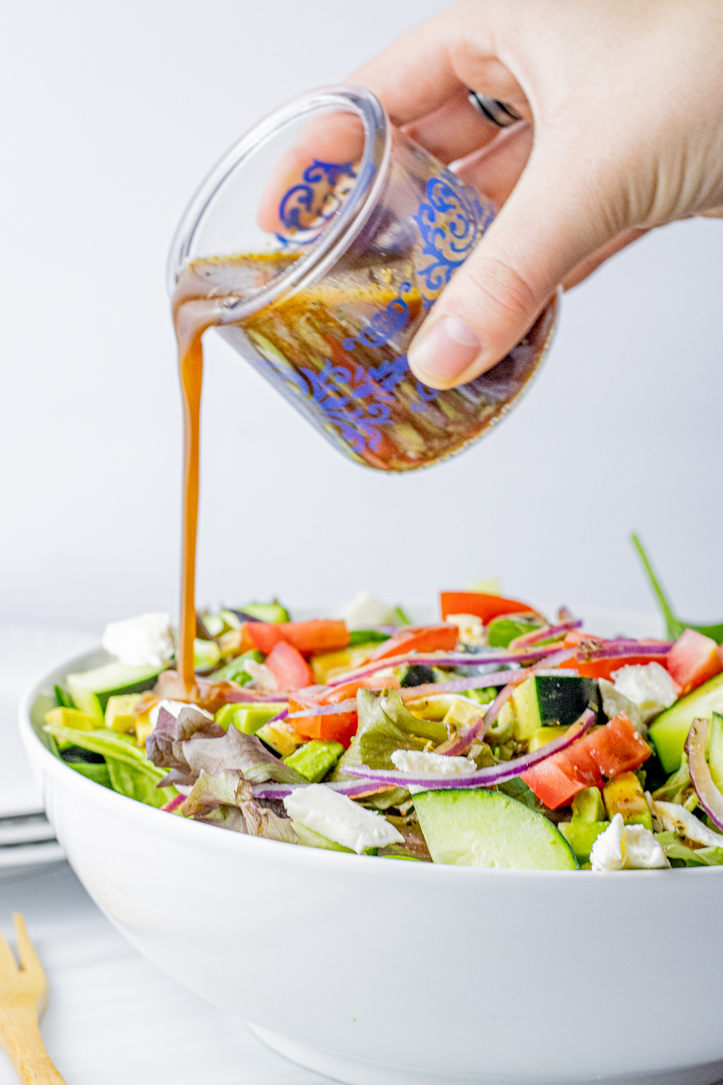 hand pouring balsamic vinaigrette over a green salad in a white bowl