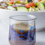 small bottle of balsamic vinaigrette with a big bowl of salad in the background