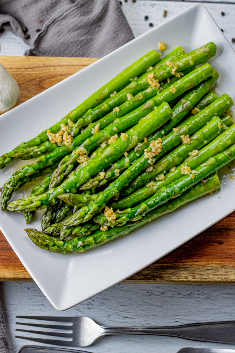 asparagus topped with garlic and butter on a white plate