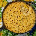 cast iron pan with cheesy corn dip with a chip scooping out some dip
