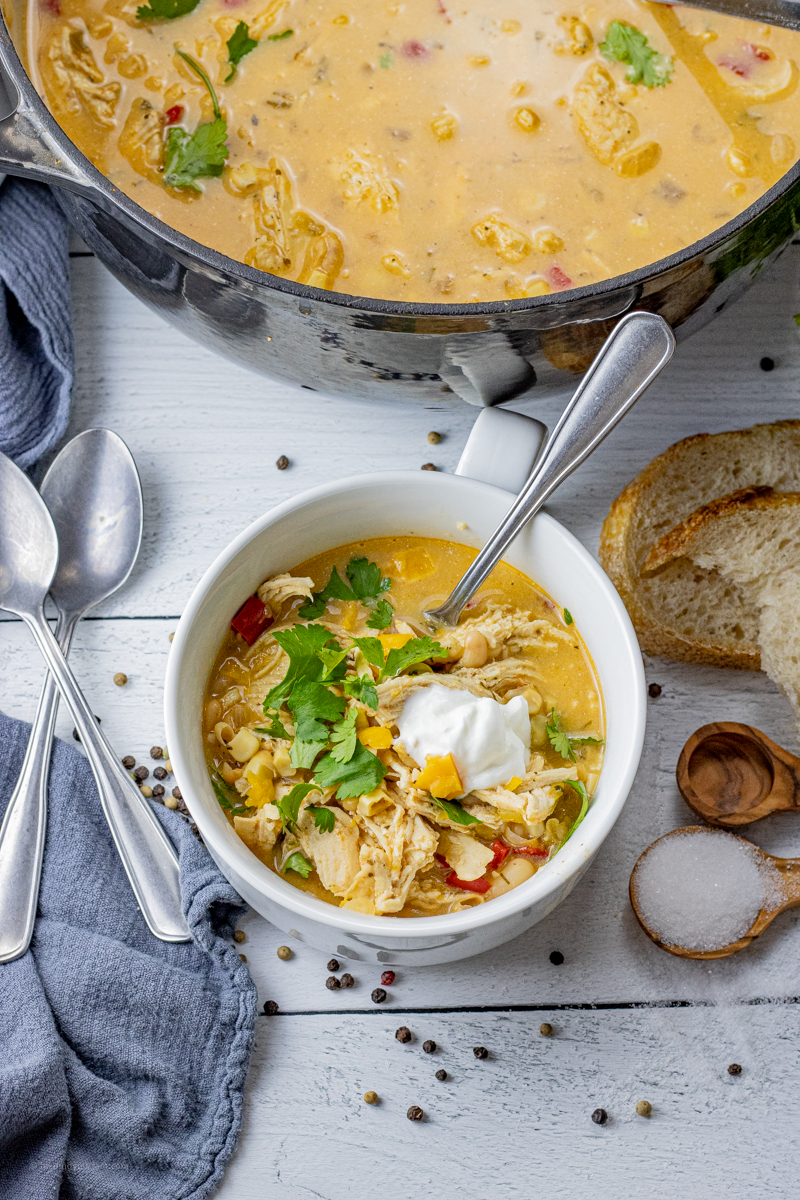 pot of white chili soup with a small white bowl filled with soup topped with sour cream and cilantro