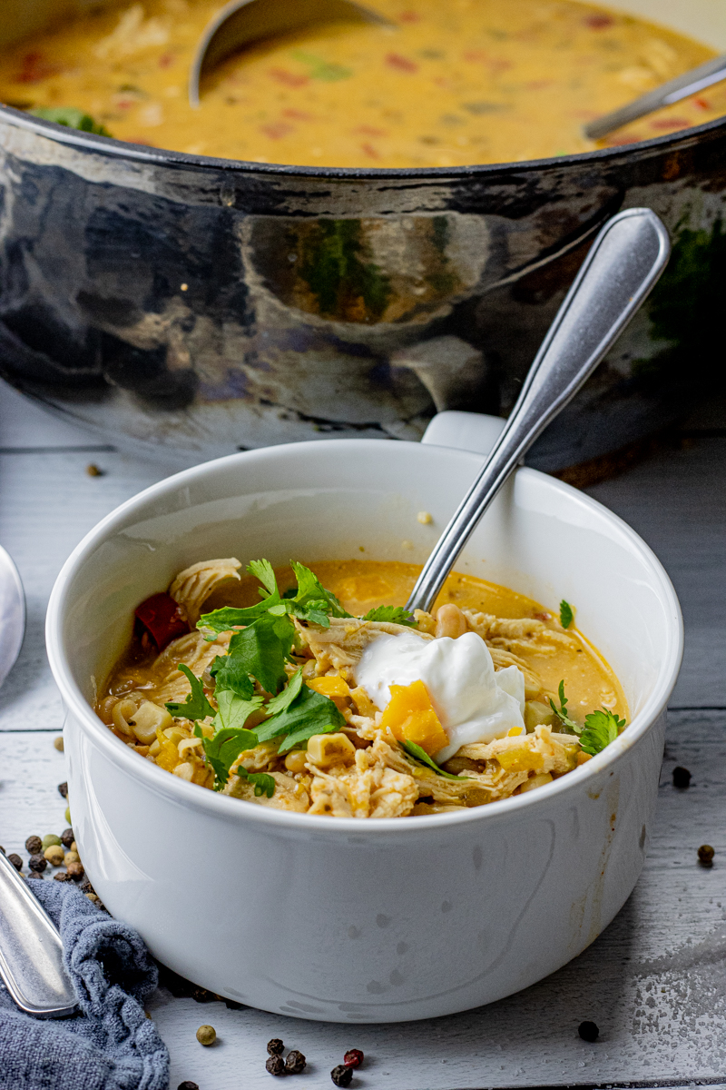 white bowl filled with white chicken chili that is topped with sour cream and cilantro