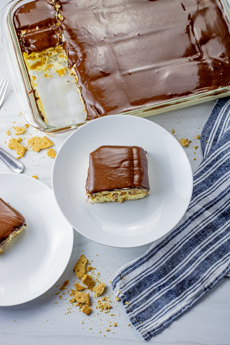 slice of layered chocolate eclair cake on a white plate with the full pan of cake in the background