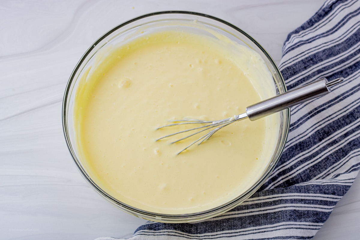 glass mixing bowl with vanilla pudding inside and a whisk in the pudding