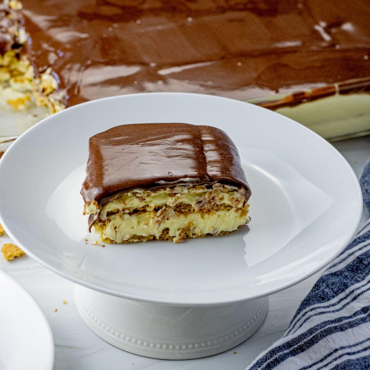 slice of layered chocolate eclair cake with graham crackers, vanilla pudding and chocolate frosting on a white plate