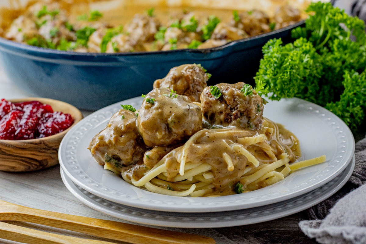 swedish meatballs in a brown gravy sauce on top of pasta on a white plate