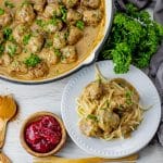pan with meatballs and gravy with a white plate next to it with pasta topped with gravy and meatballs