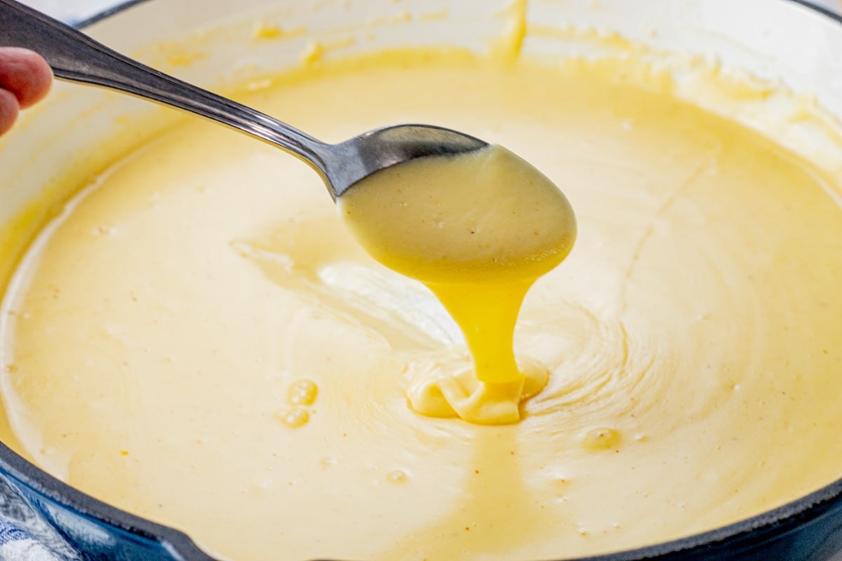 spoon dripping nacho cheese sauce into a pan