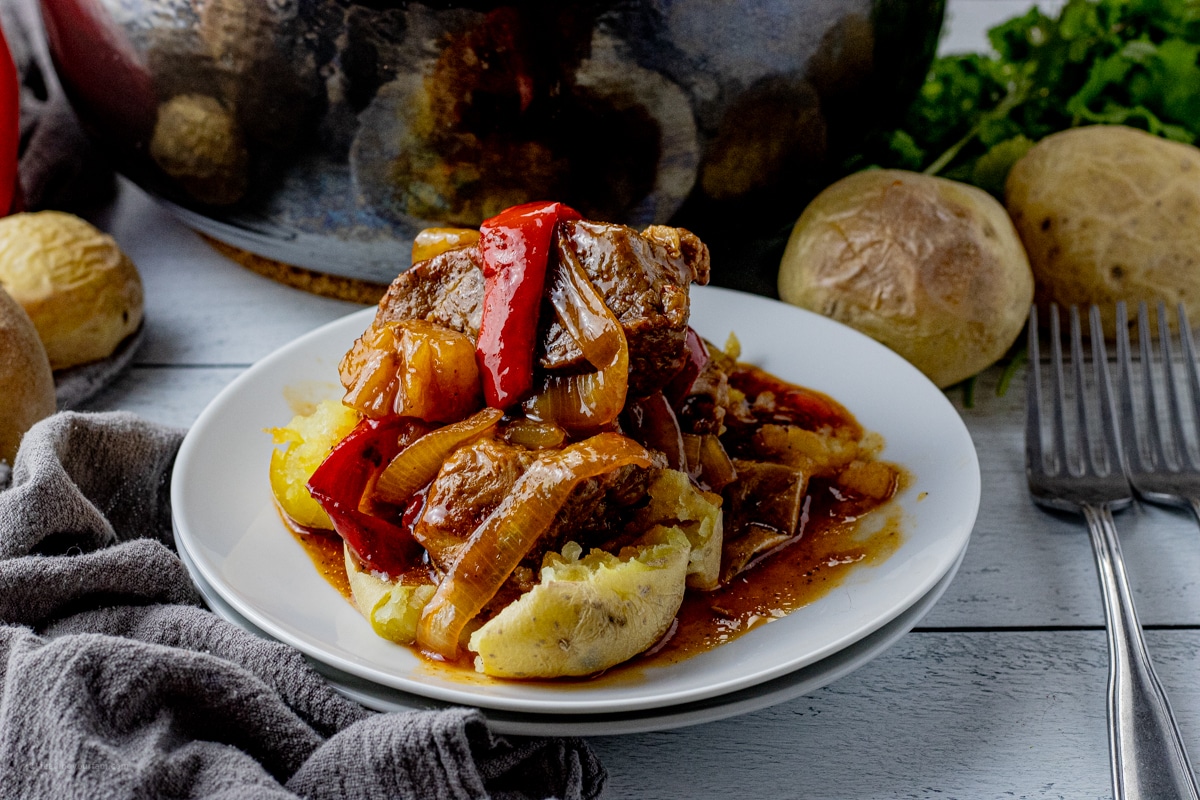 cooked boneless pork ribs with peppers and onions over potatoes