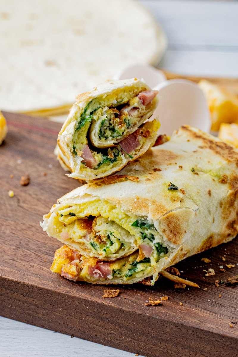 cooked eggs ham, spinach and cheese rolled up in a flour tortilla