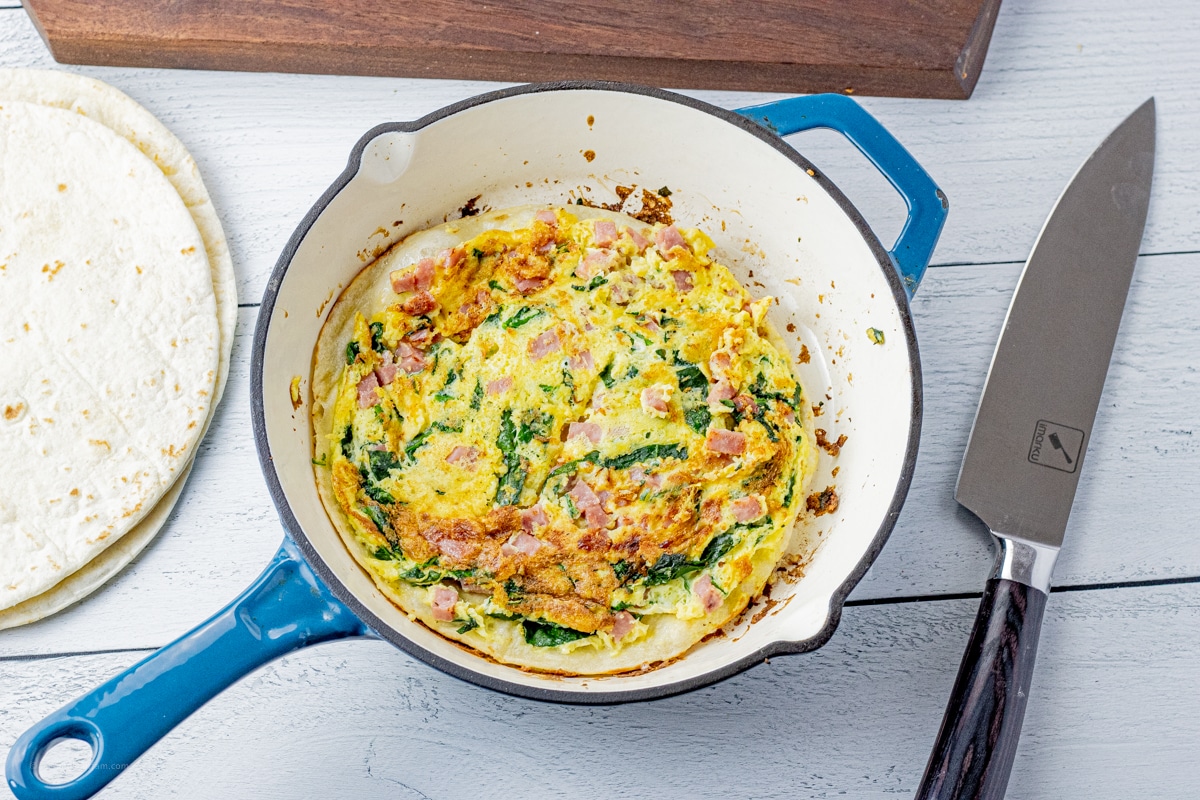 cooked, eggs, ham and cheese cooked on top of a flour tortilla in a pan