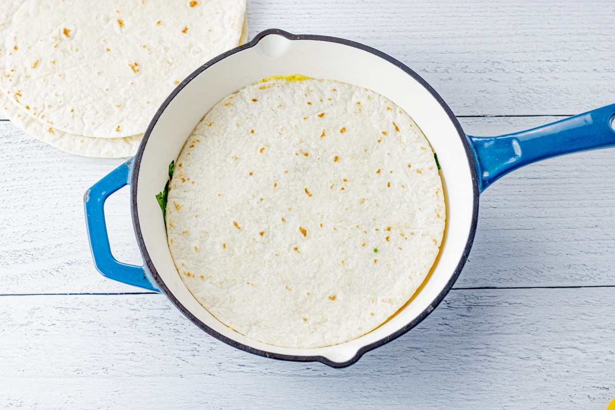 uncooked tortilla over eggs in a pan