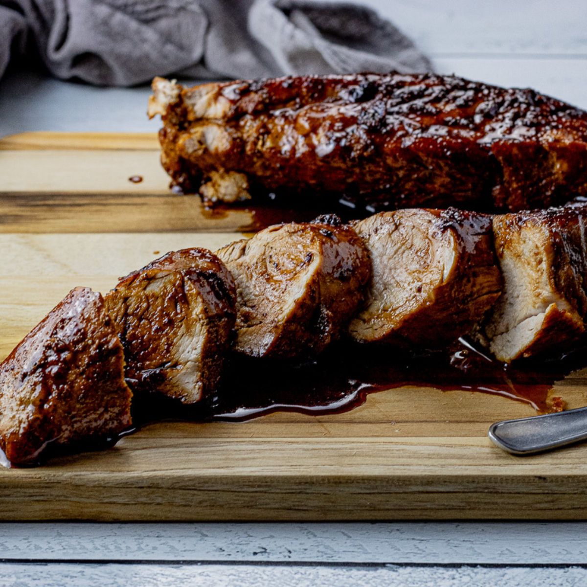 two pork tenderloins on a wooden cutting board, one sliced and drizzled with maple glaze