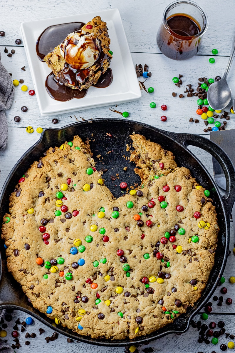 chocolate chip cookie in a cast iron skillet with a piece cut out on a plate and topped with vanilla ice cream