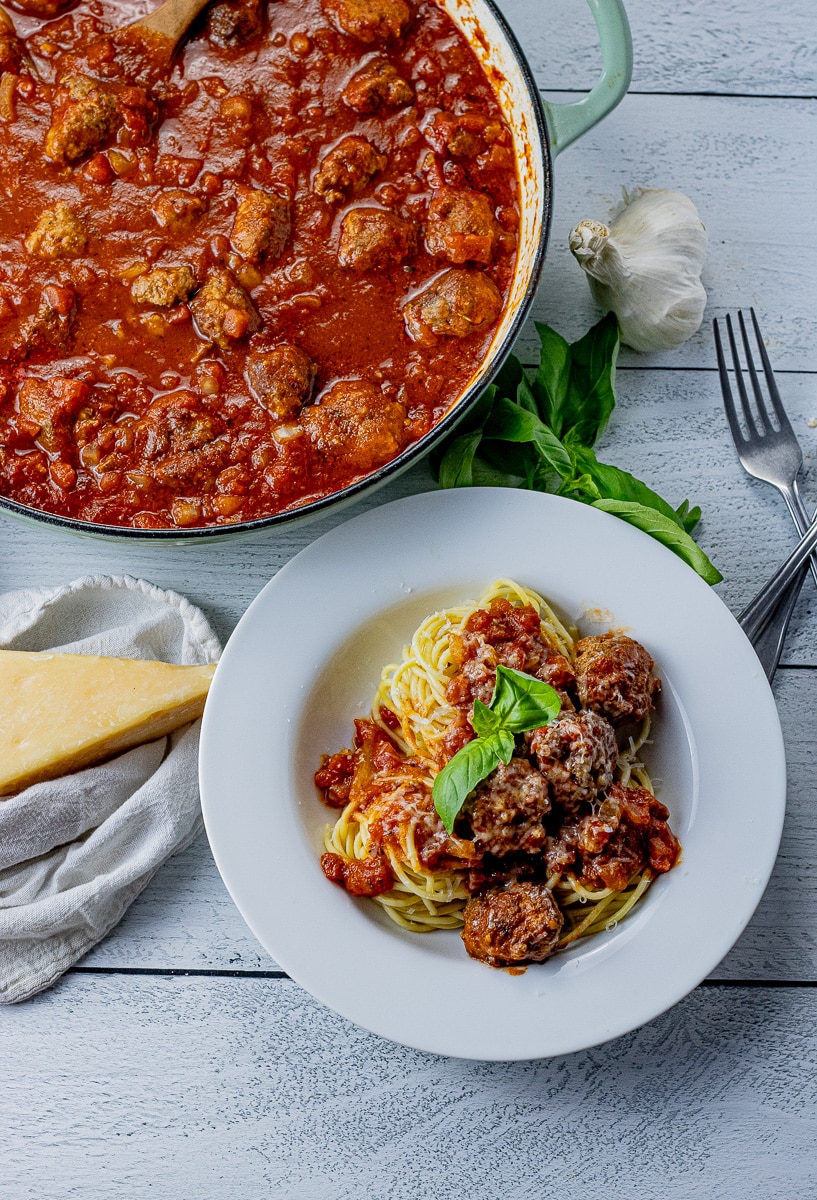 spaghetti and meatballs in a large pan with a small bowl with some and basil on the side