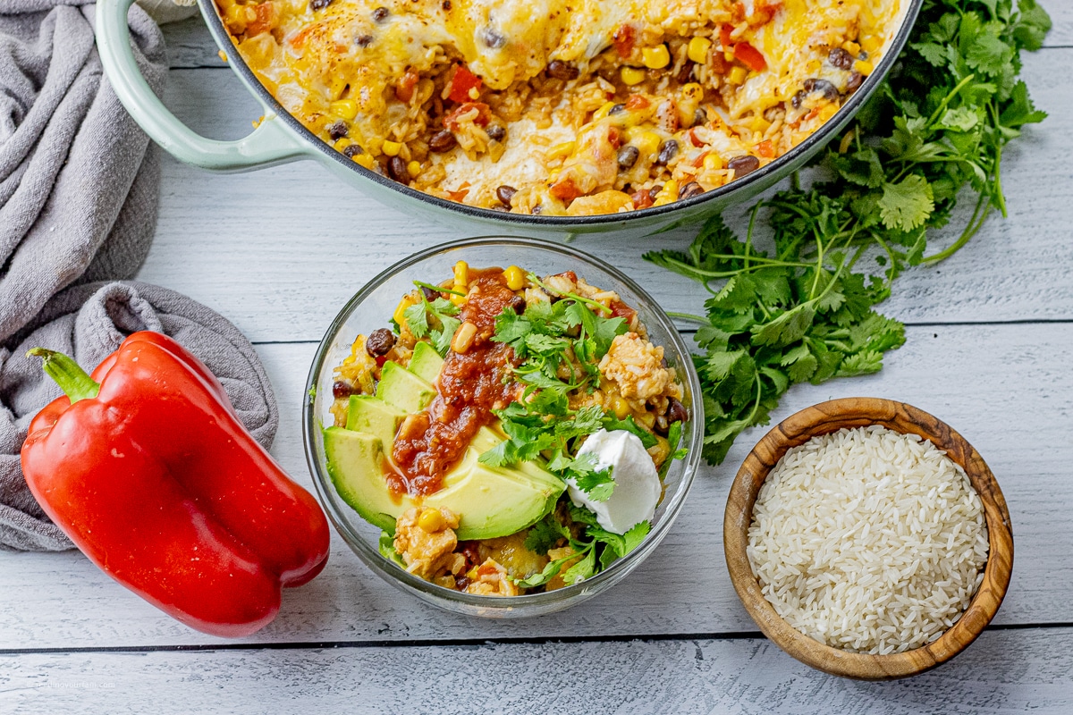 glass bowl with rice, chicken, topped with sour cream, avocado slices, salsa and cilantro