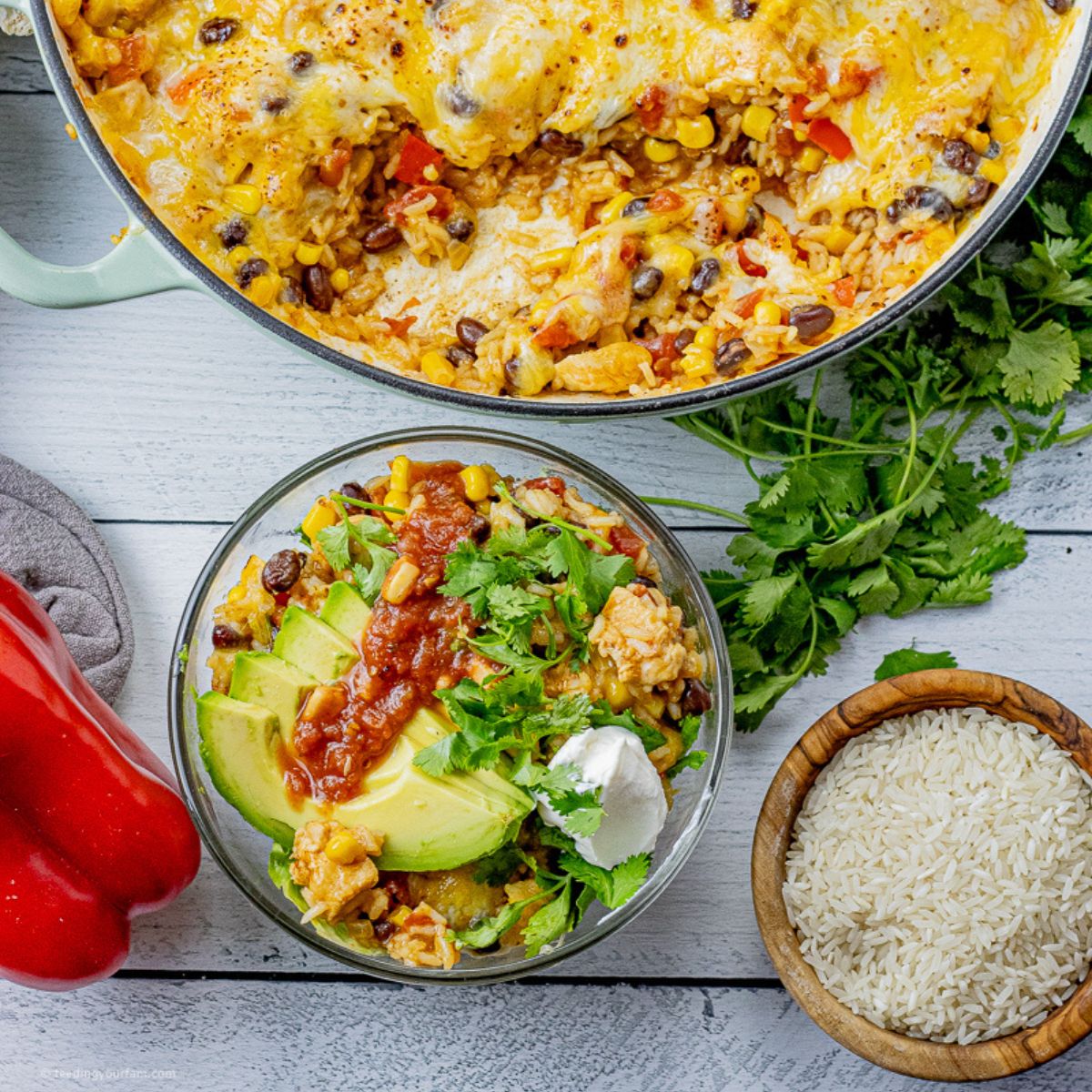 bowl of rice, chicken, peppers, onions, beans and corn topped with avocados, sour cream and salsa