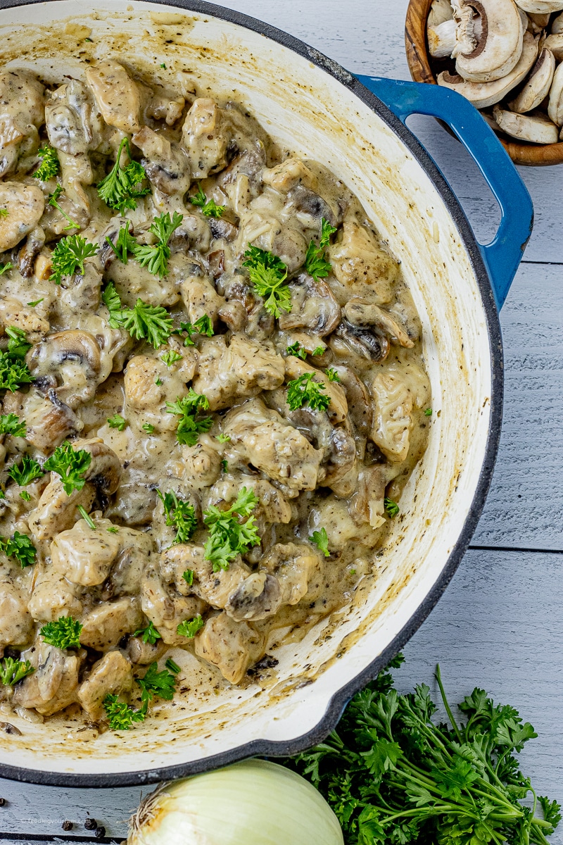 diced chicken with sliced mushrooms and onions in a creamy sauce in a cast iron pan, only half the pan is showing