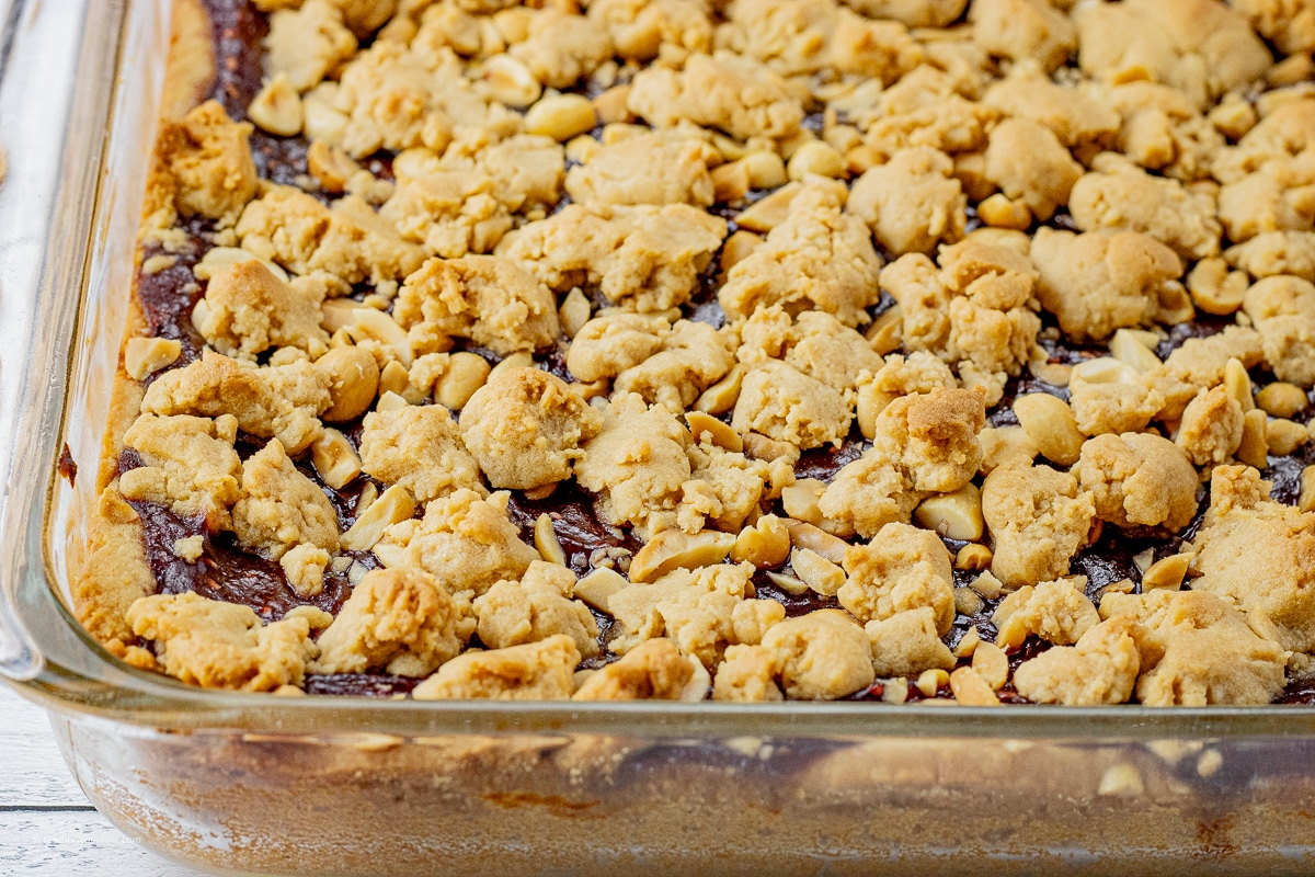 glass pan with cookie bars made with peanut butter crust, a layer of jelly and pieces of peanut butter cookie dough on top