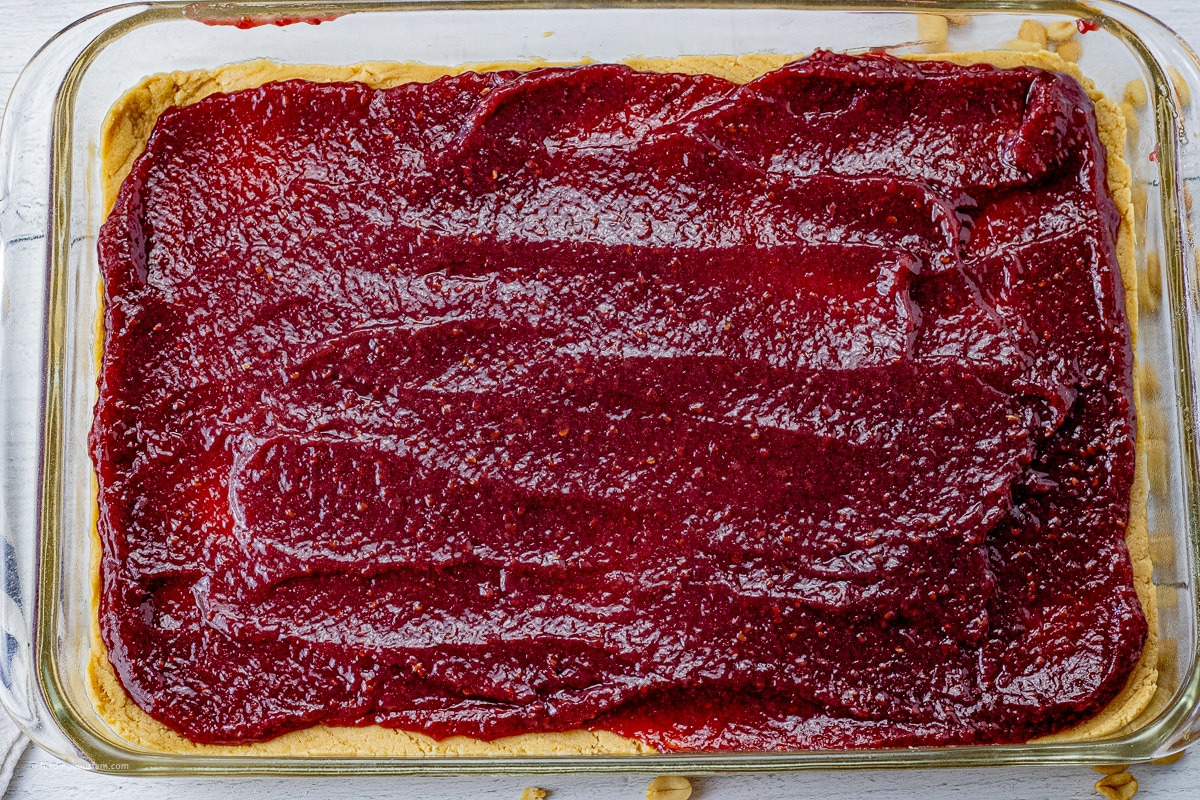 glass baking dish with peanut butter dough on the bottom and a layer of raspberry jam on top