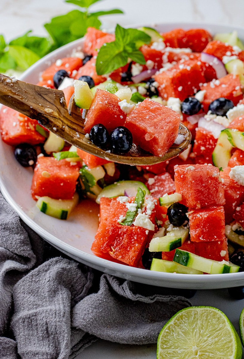 wooden spoon scooping up cubed watermelon with blueberries and feta cheese