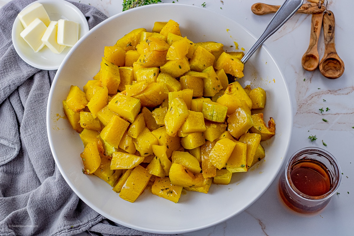cubes of butternut squash that have been roasted and placed into a white serving bowl.