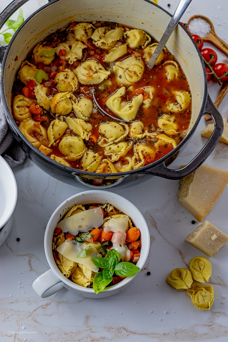 big pot of vegetable tortellini soup with a bowl filled with it next to it.