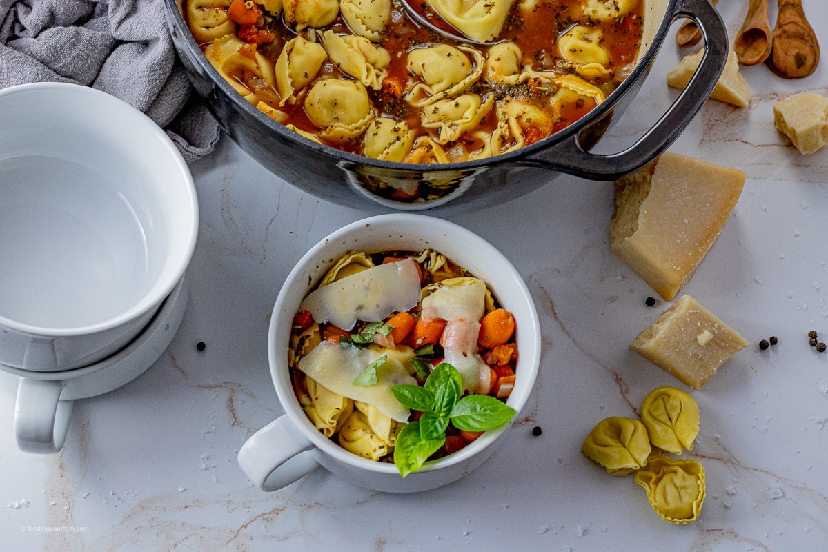 bowl filled with tortellini tomato soup with a big pot of the same soup in the back