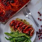sliced chicken in a cranberry sauce on top of rice with a side of green beans