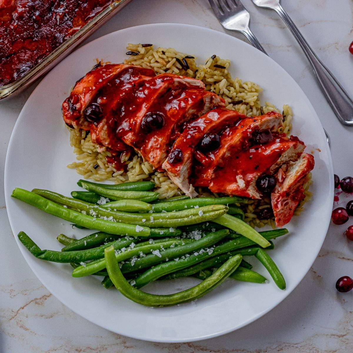 sliced chicken in a cranberry sauce over rice with a side of green beans