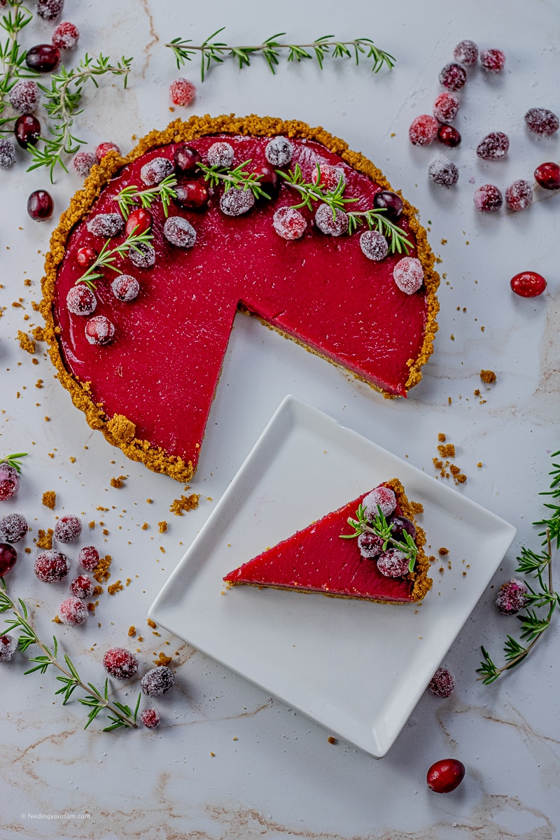 cranberry tart topped with sugared cranberries with a slice out on a white square plate