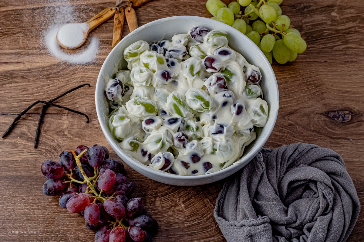 This Grape Salad Recipe is a simple and quick side dish that is loaded with red and green grapes in a creamy dressing covered in brown sugar and pecans. Perfect for potlucks and family get togethers! red and green grape salad topped with a cream cheese dressing in a white serving bowl