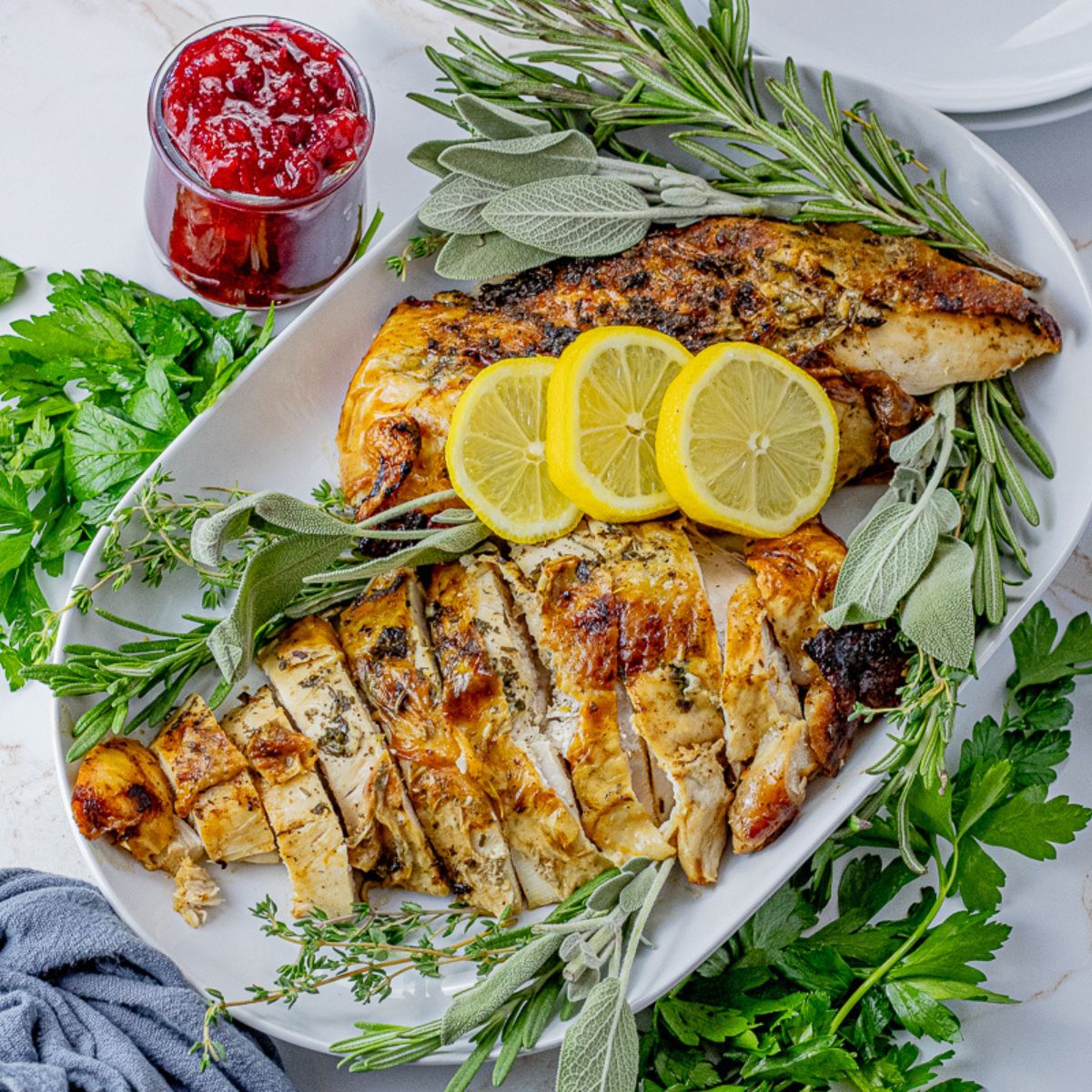 sliced turkey breast on a white serving platter with fresh herbs and lemon slices