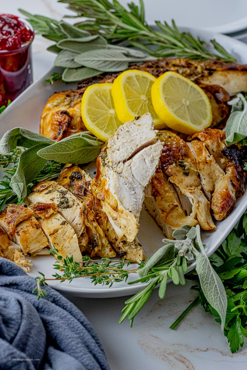 sliced turkey breast on a white serving platter with lemon slices and fresh herbs surrounding it