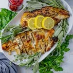 sliced turkey breast on a white serving plate with lemon slices and herbs