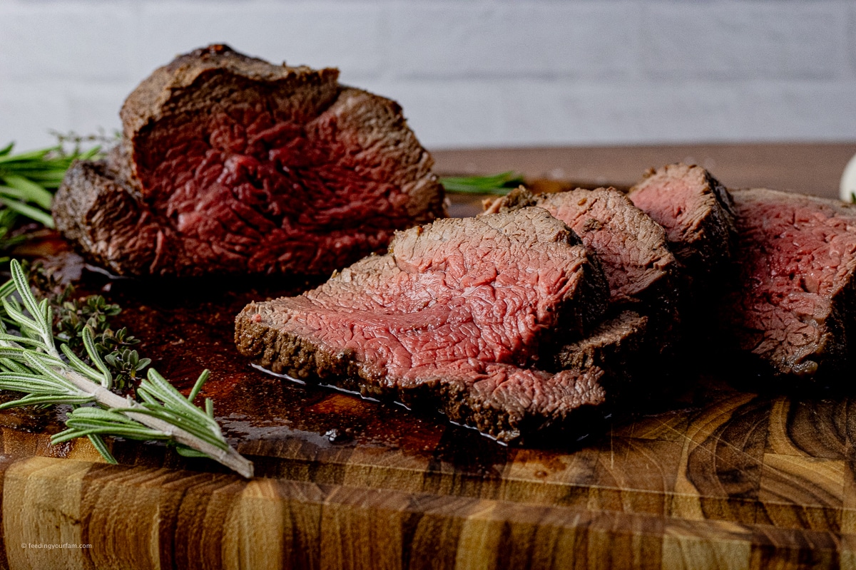 sliced beef tenderloin cooked medium rare on a wooden cutting board