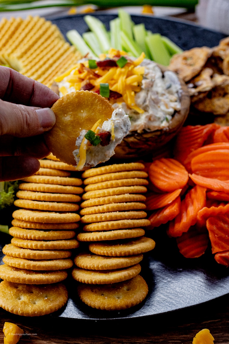 hand holding a round cracker with cream cheese dip on it