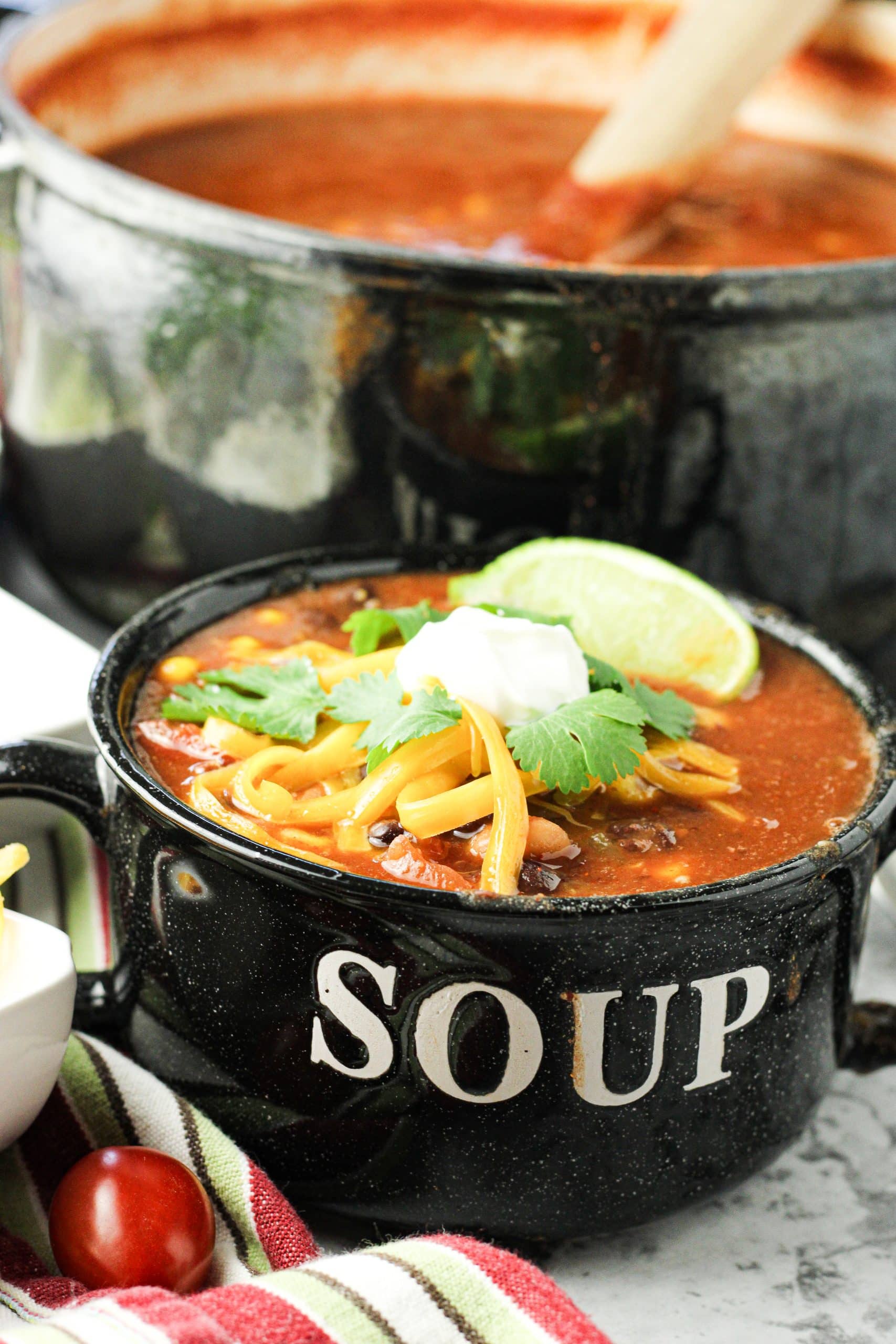 bowl with the word soup on it filled with taco soup topped with sour cream, shredded cheese and cilantro to make 8 can taco soup recipe