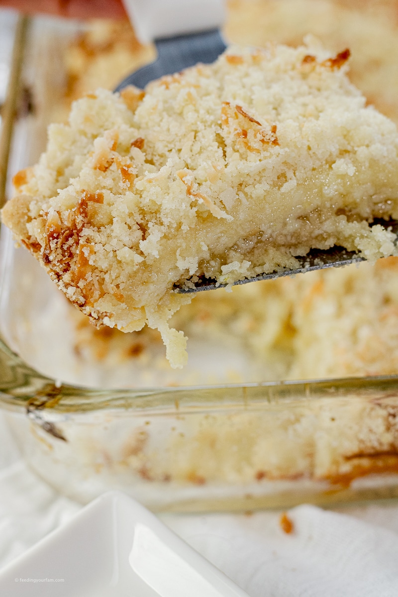 spatula lifting up a piece of a lemon coconut bar from a glass baking pan