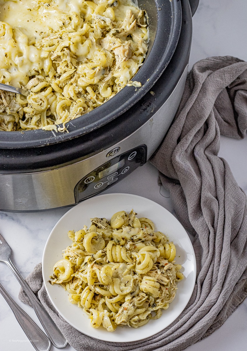 slow cooker with twisted pasta, shredded chicken and pesto sauce on a white plate