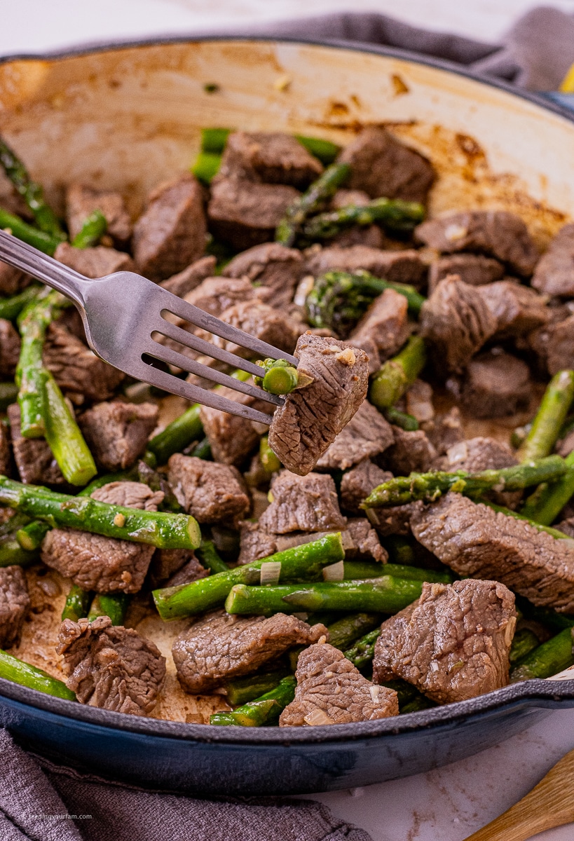 a fork holding up a piece of garlic butter steak bite over a cast iron pan