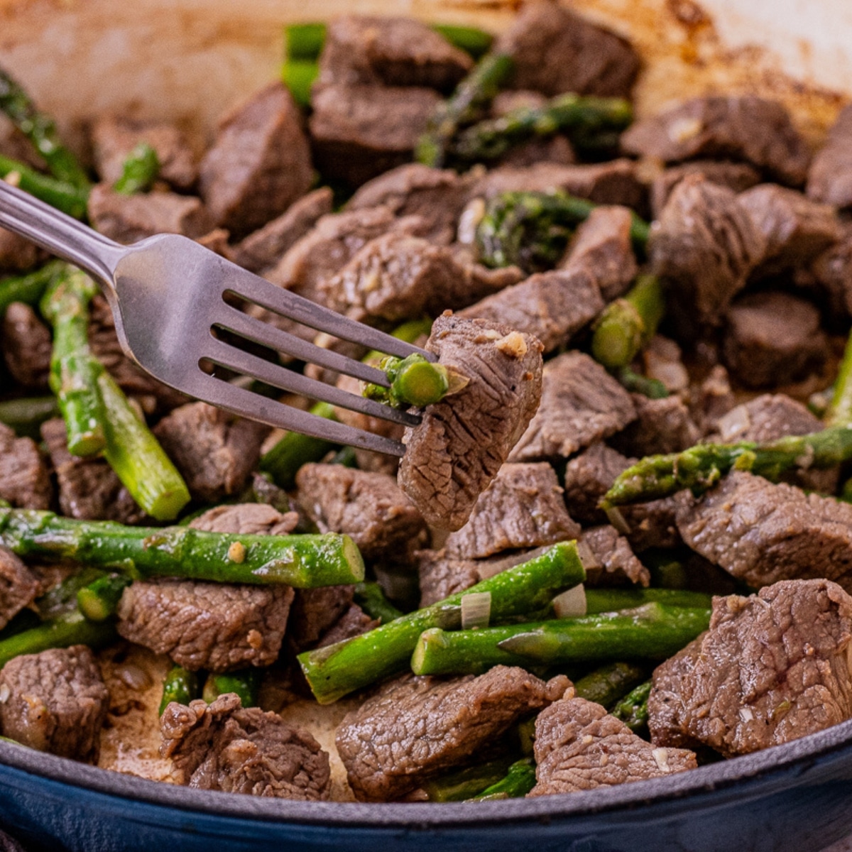 fork holding a piece of asparagus with a small piece of steak