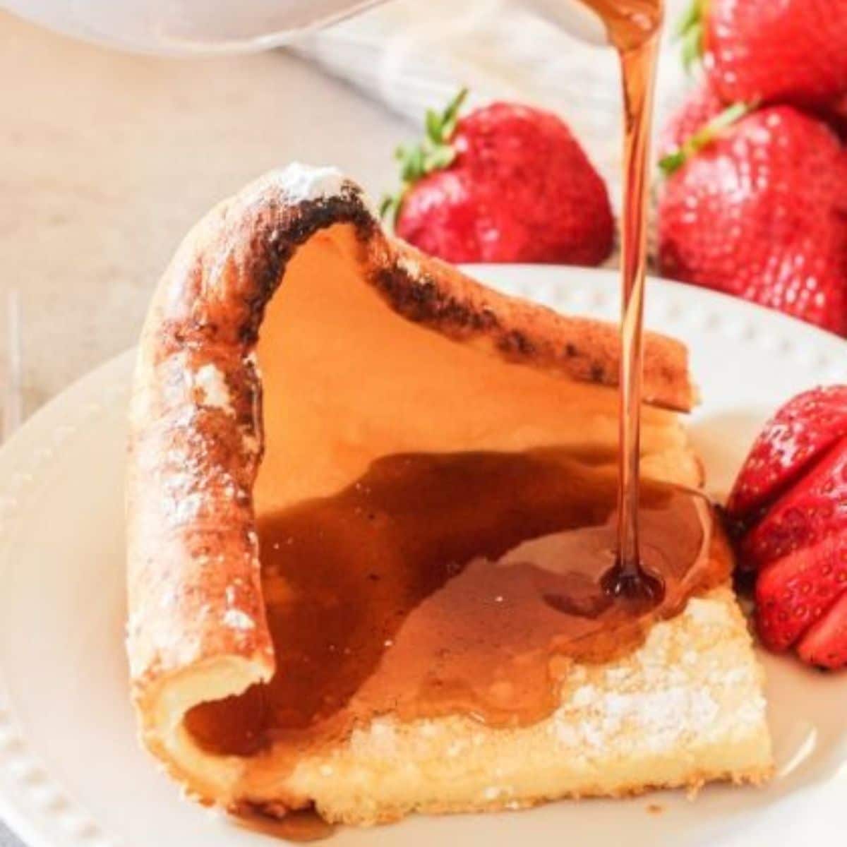 german pancake slice with syrup pouring over it