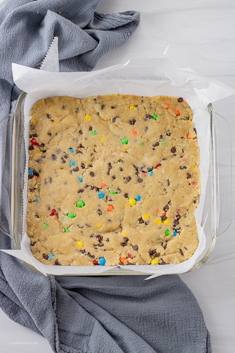 uncooked chocolate chip cookie dough bars with mini chocolate candy pieces pressed into a square baking pan