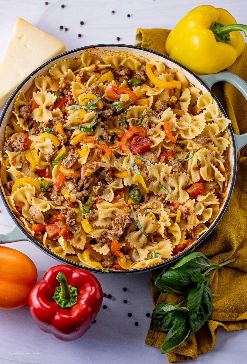 Easy Italian Sausage and Pepper skillet meal is so easy to make and comes together so quickly! You are going to love the flavors and simplicity! peppers, bowtie pasta and sausage in a round pan