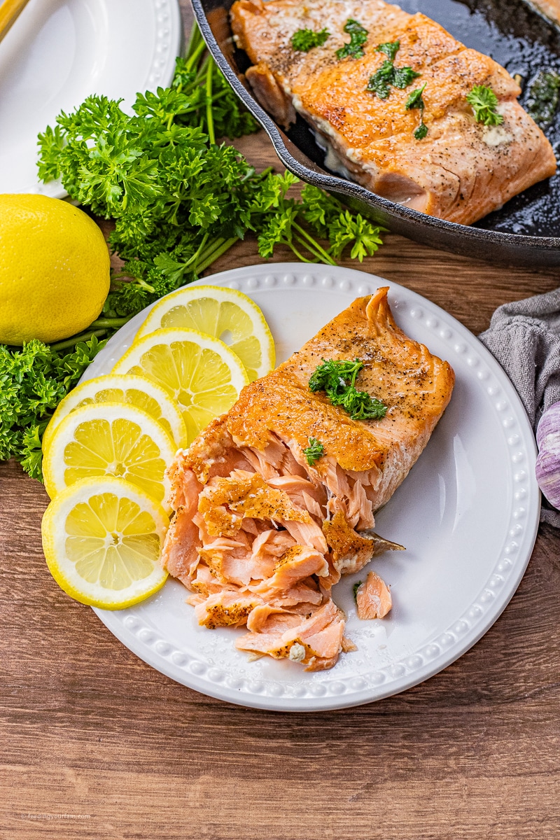 cast iron skillet salmon on a white plate with the salmon flaked a little bit with some lemon slices