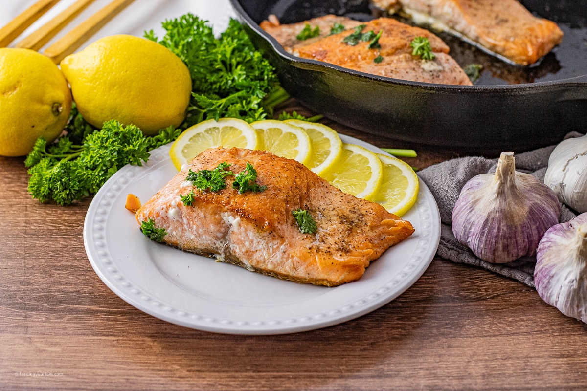 skillet cooked salmon filet on a white circle plate with some lemon slices
