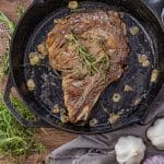 ribeye in a cast iron pan with thyme, rosemary and sliced garlic