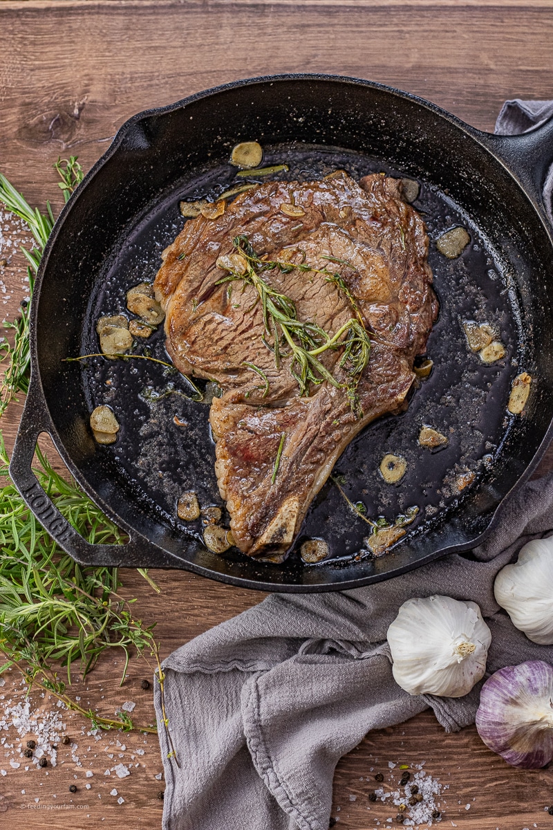 ribeye in a cast iron pan with thyme, rosemary and sliced garlic